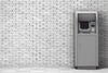 a grey automated banking machine against a grey brick wall